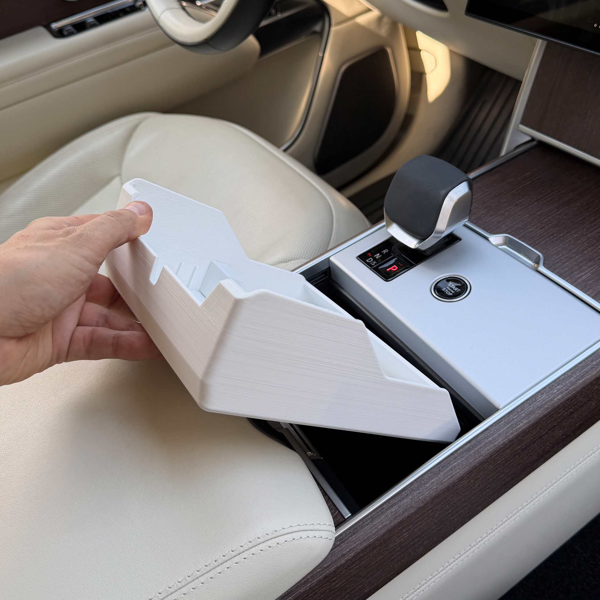 Hand lowering the white organizer tray into the hidden compartment beneath the Range Rover cupholders