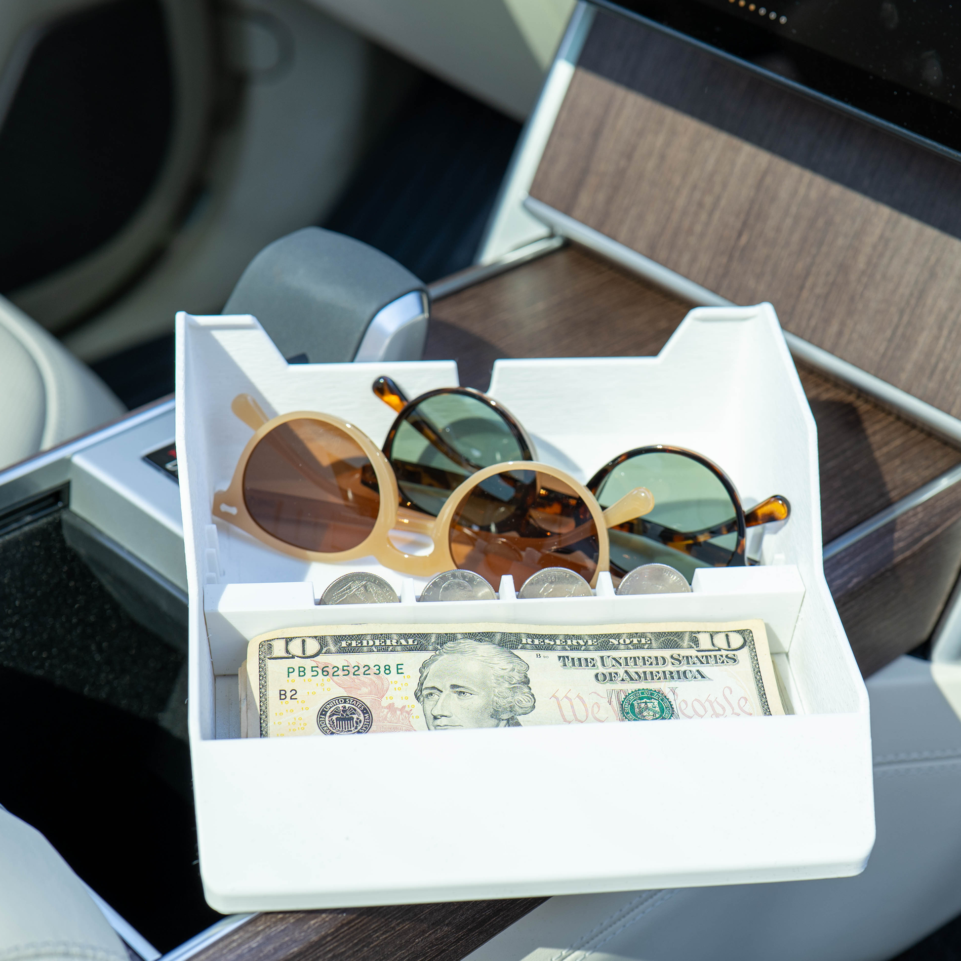 Three pairs of sunglasses, coins and cash stored side by side in the white Range Rover Hidden Storage Organizer Tray